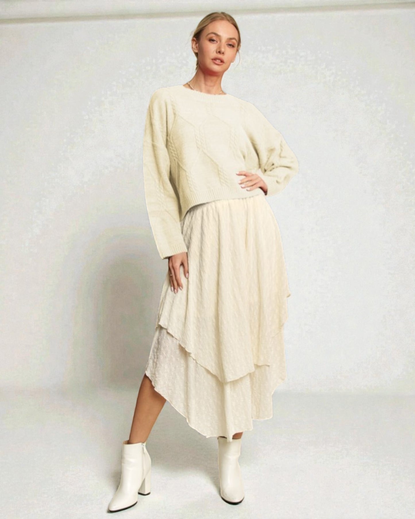 Woman wearing a beige sweater and skirt with white boots on a plain background