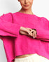 A close-up of a model wearing a bright hot pink cropped cable-knit sweater with voluminous balloon sleeves, paired with cream-colored pants.