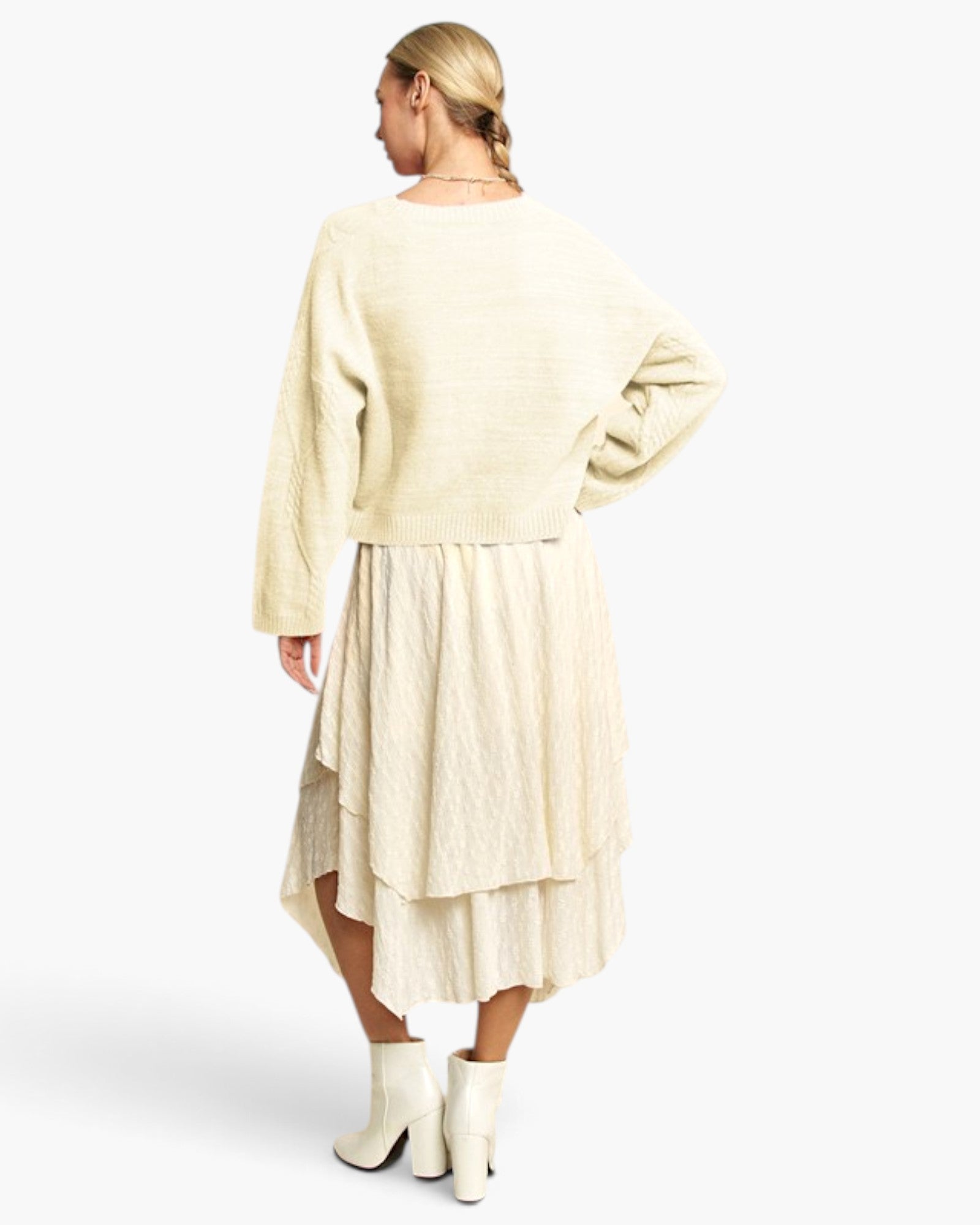 A woman shown from the back wearing a cream-colored textured knit long-sleeve top and matching textured midi skirt, paired with cream ankle boots, against a light gray studio background.