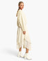 A model is shown from the back wearing a cream-colored textured knit sweater and matching layered asymmetrical skirt, paired with white ankle boots, against a plain light gray studio background.