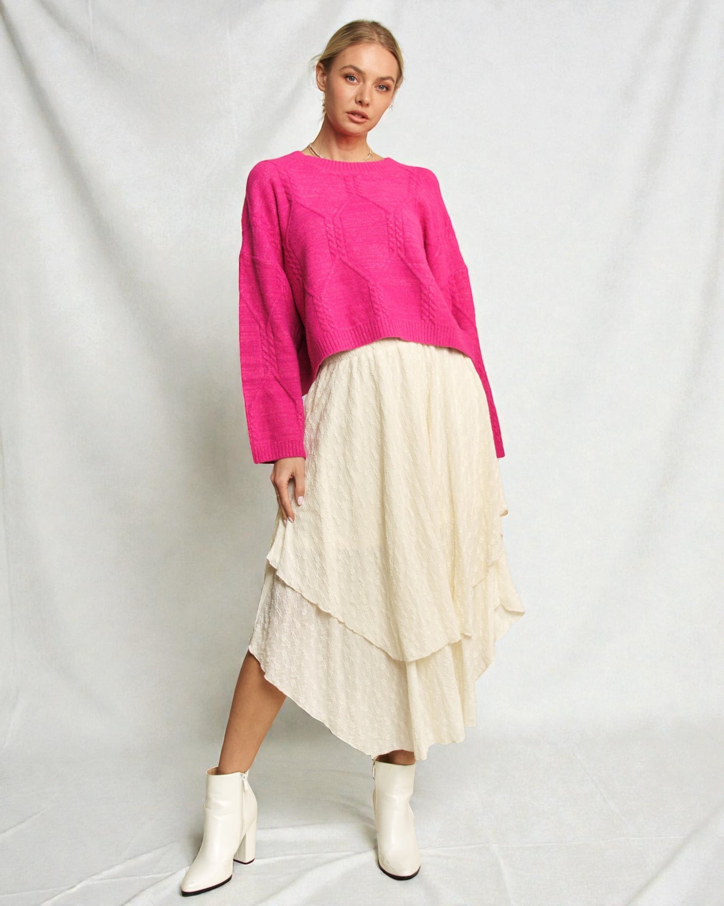 Woman wearing a bright pink sweater and cream skirt on a white background