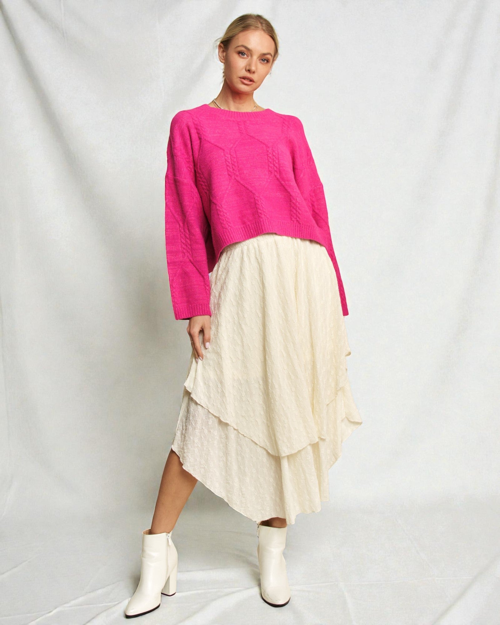 Woman wearing a bright pink sweater and cream skirt on a white background