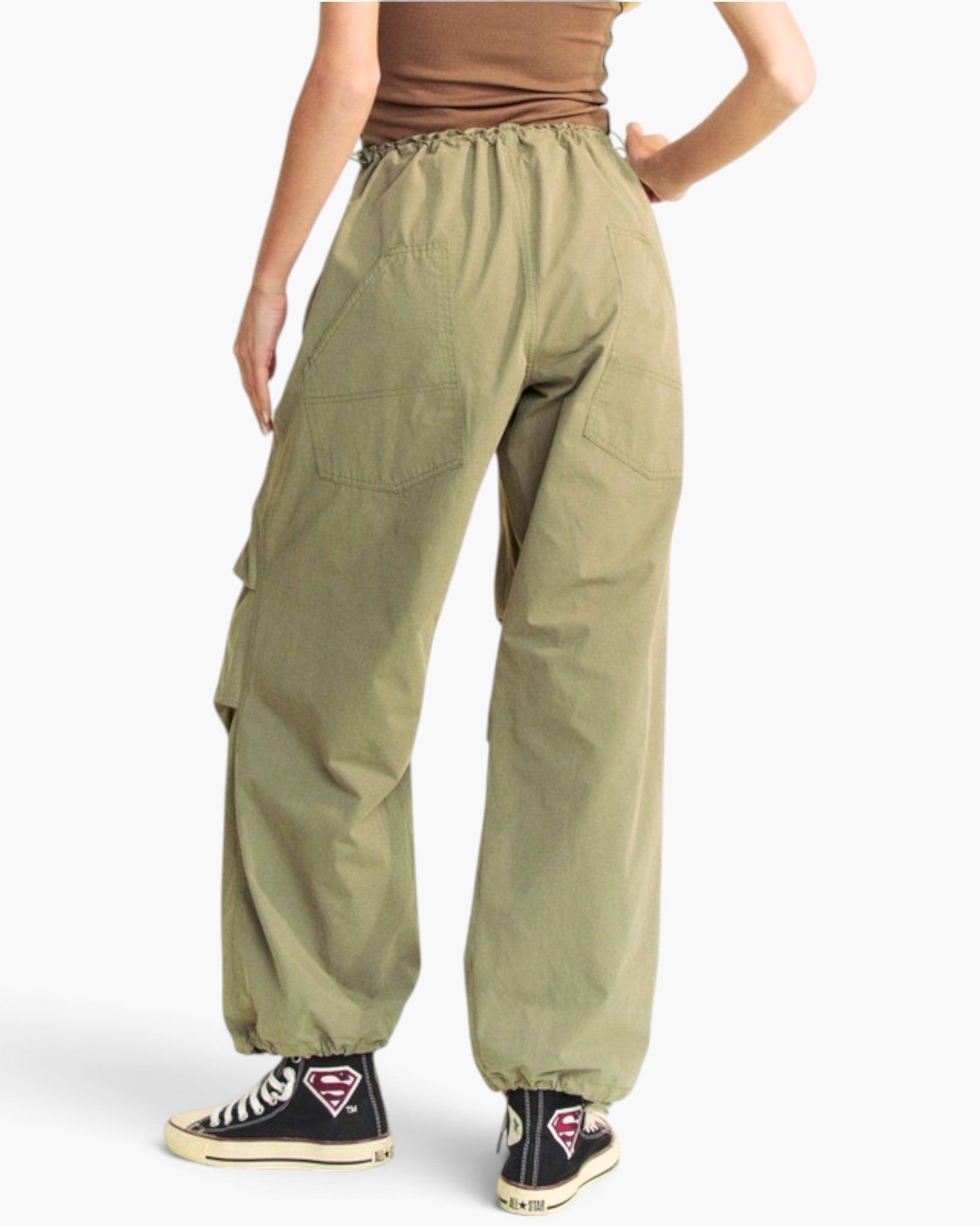A person shown from the back wearing loose olive green cargo-style pants with an elastic waistband and elastic cuffs, paired with black sneakers against a plain light background.