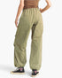 A person shown from the back wearing loose olive green cargo-style pants with an elastic waistband and elastic cuffs, paired with black sneakers against a plain light background.