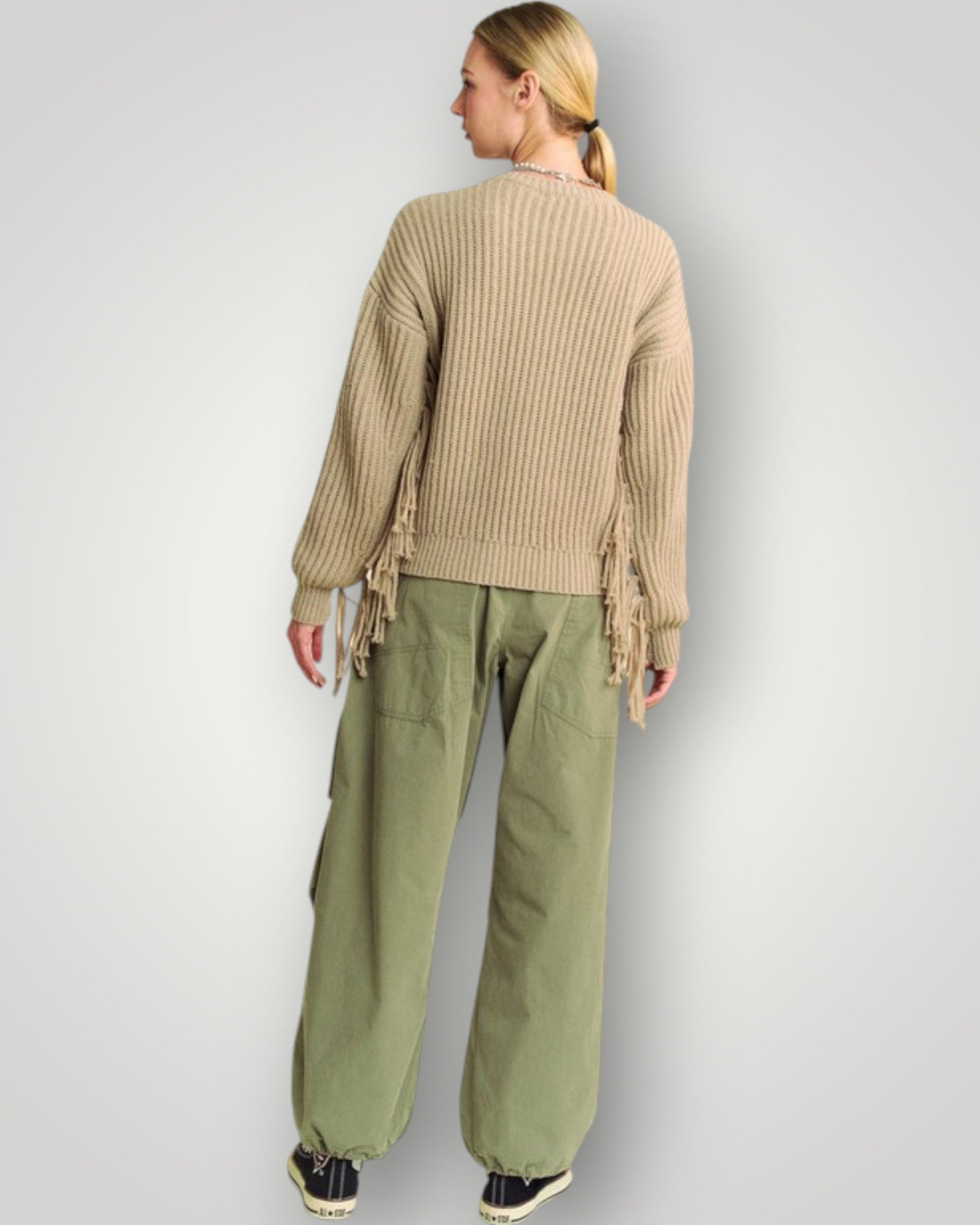 Person wearing a beige ribbed sweater and green pants on a light gray background