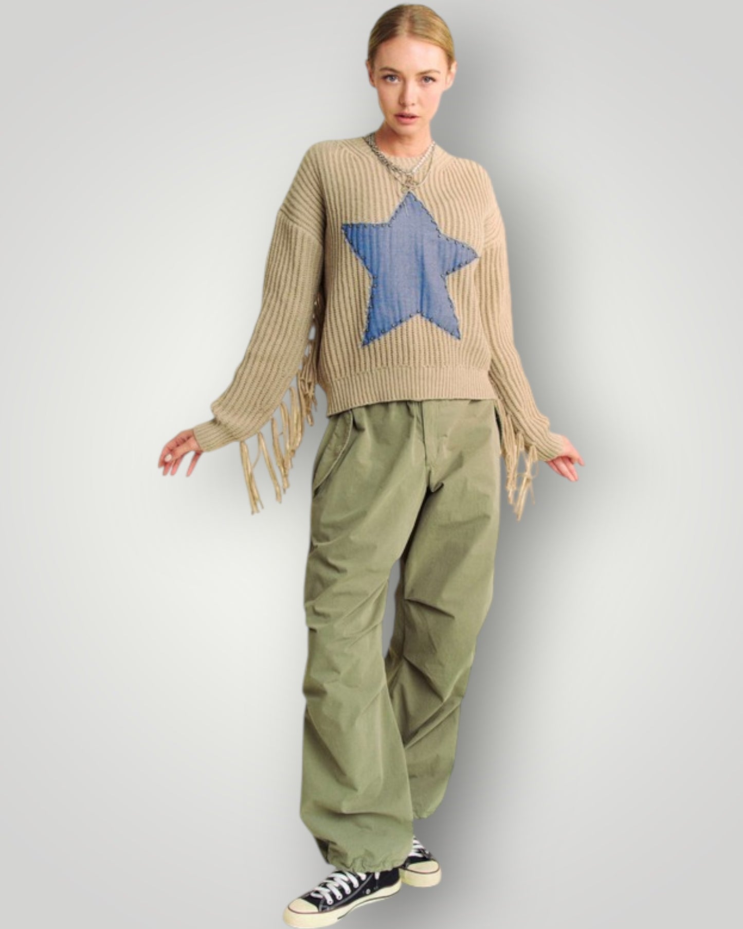 Person wearing a beige sweater with a blue star and green pants on a light gray background
