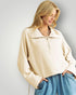 Woman wearing a beige jacket and blue jeans against a plain background