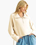 A woman wearing a cream-colored, oversized quarter-zip sweatshirt with a wide collar and blue jeans, photographed against a solid white background.