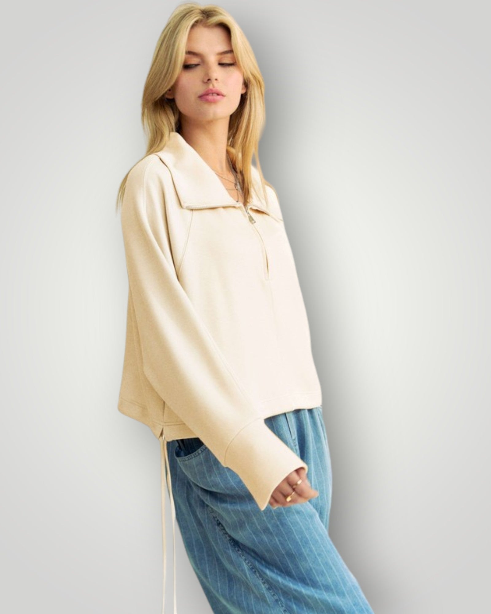 Woman wearing a beige jacket and blue jeans against a plain background