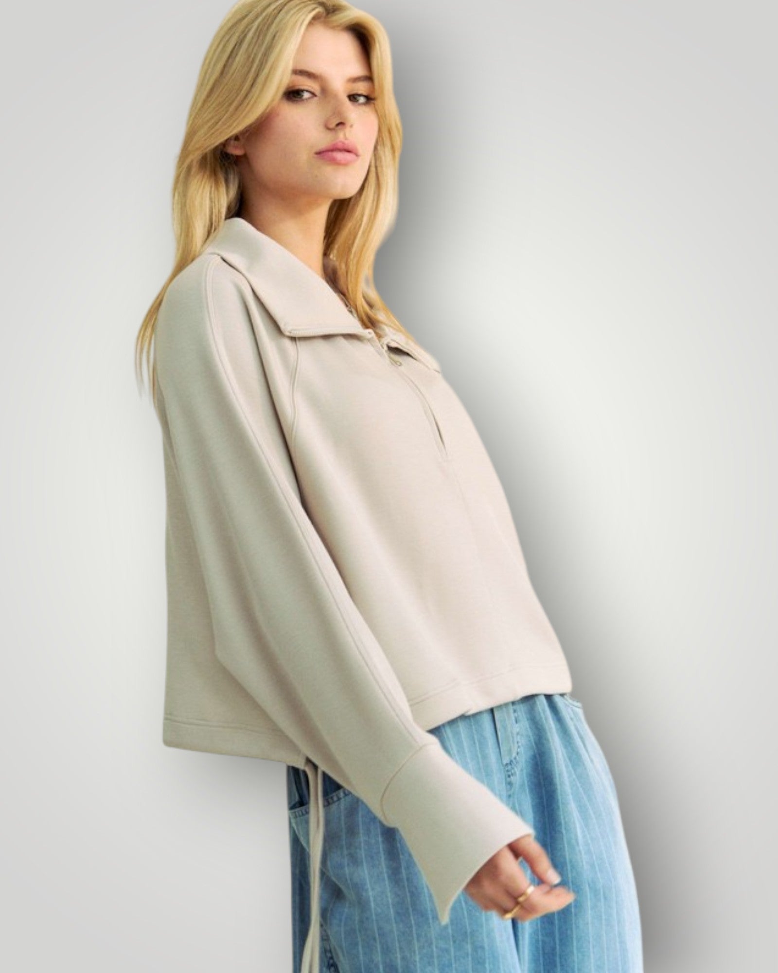 Woman wearing a beige jacket and blue jeans against a plain background