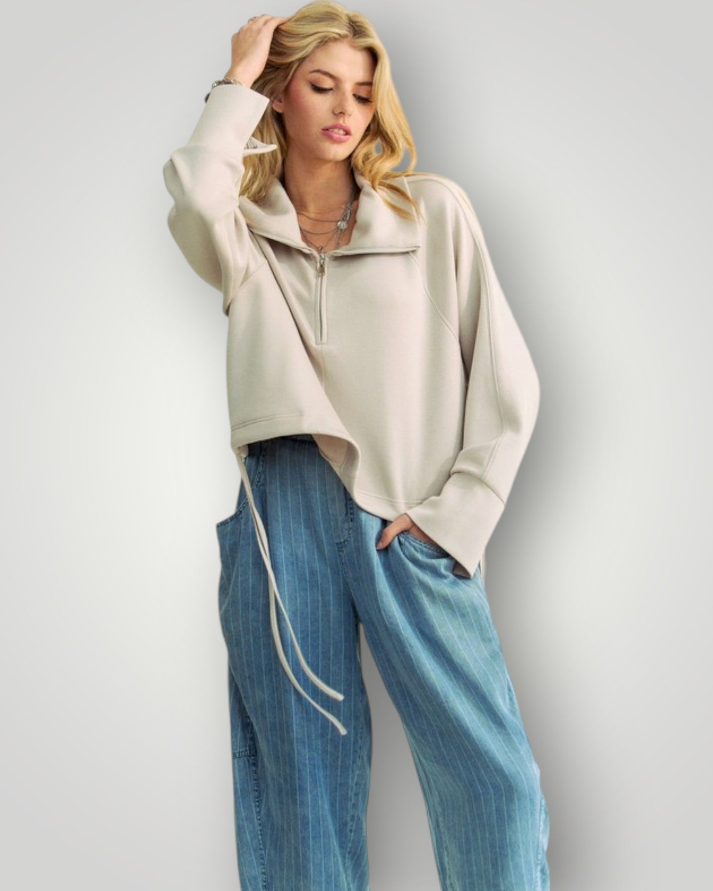 Woman wearing a beige sweater and blue jeans against a plain background