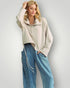 Woman wearing a beige sweater and blue jeans against a plain background