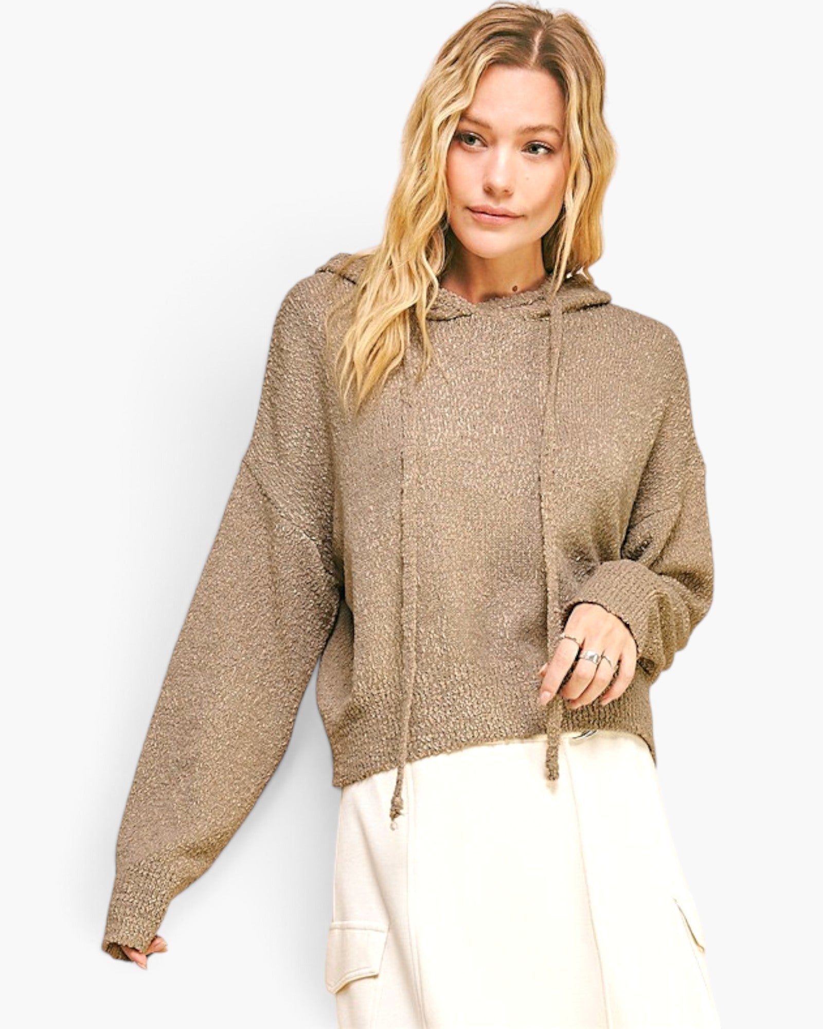 A woman wearing a textured, oversized knit hoodie in a warm taupe-brown color, paired with cream cargo pants, against a plain white studio background.