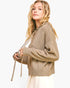 A woman wearing a textured, oversized knit hoodie in a warm taupe-brown color, holding the drawstrings. The background is a clean, solid white.