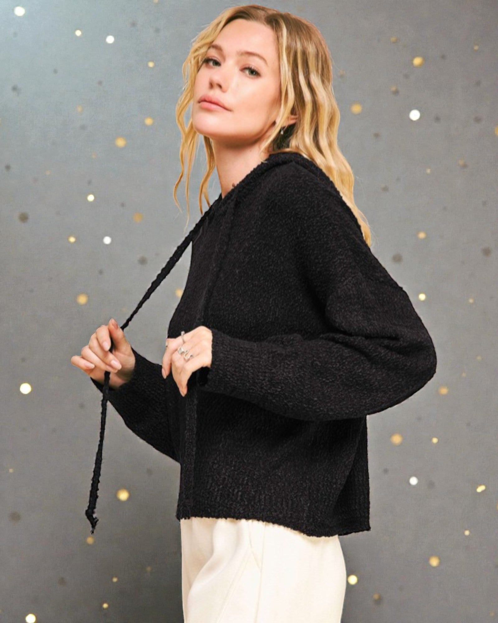 Woman wearing a black sweater against a gray background with gold dots