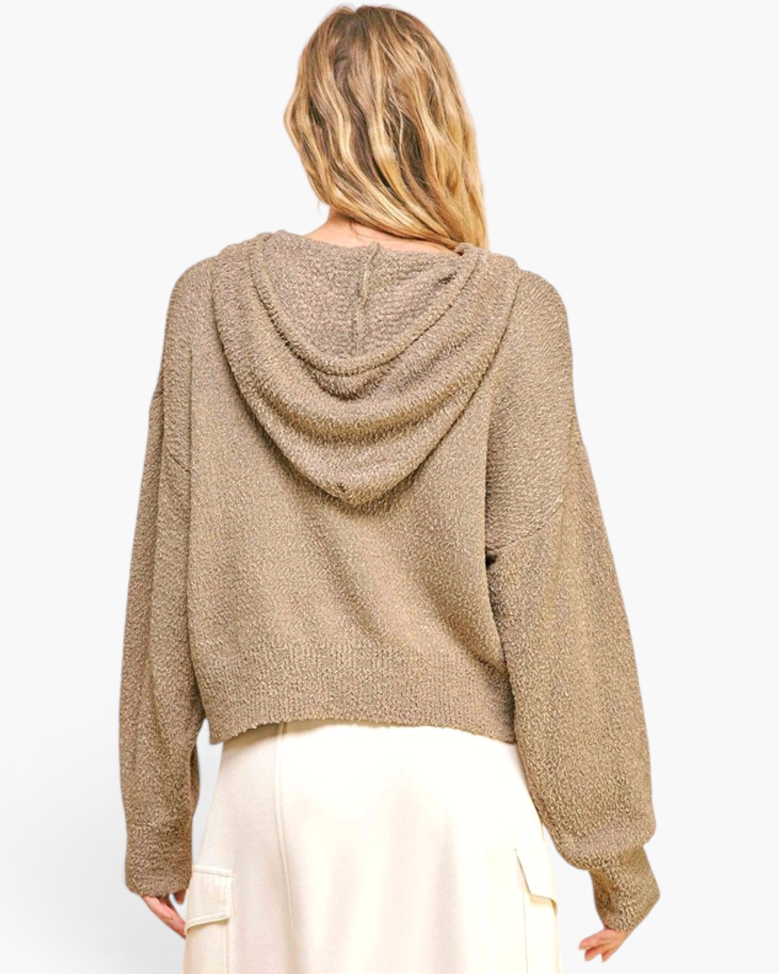 A woman shown from the back wearing a textured, cropped knit hoodie in a warm taupe-brown color, paired with cream-colored pants, against a plain light gray background.