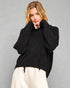 Woman wearing a black sweater and white pants against a gray background