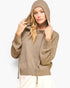 A woman wearing a textured, heathered taupe-brown hooded pullover sweater with drawstrings, posing against a light gray studio background.