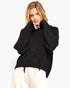 A woman wearing a black fuzzy knit sweater with a high turtleneck and drawstring hem, paired with cream-colored pants, against a plain white background.