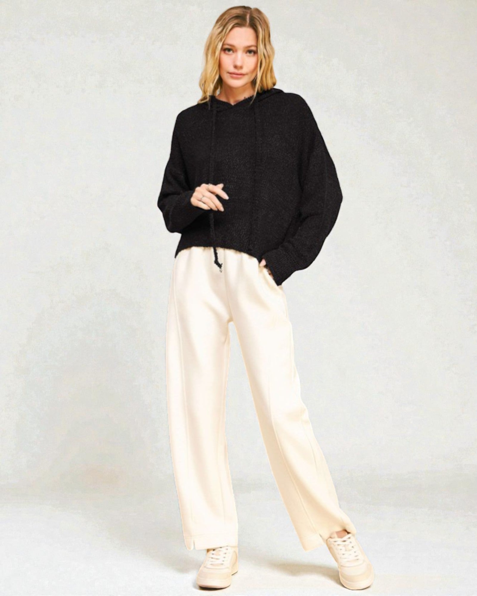 Person wearing a black sweater and white pants on a plain background