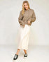 Woman wearing a brown hoodie and white pants against a white background