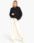 A woman modeling a black knit cropped hoodie and cream wide-leg sweatpants with cream sneakers, set against a plain light gray studio background.