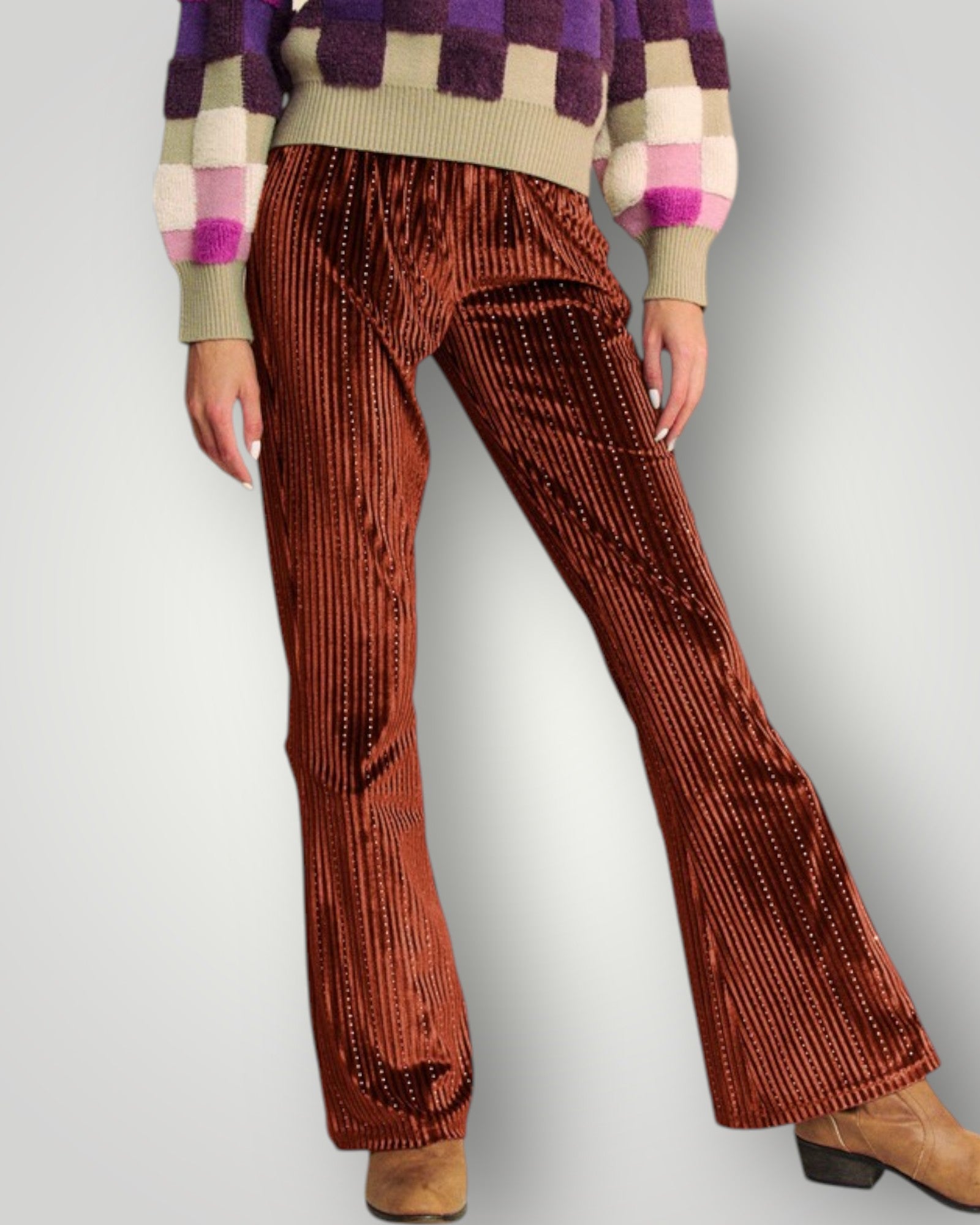 Brown pleated pants worn with a colorful sweater on a plain background
