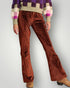 Brown pleated pants worn with a colorful sweater on a plain background