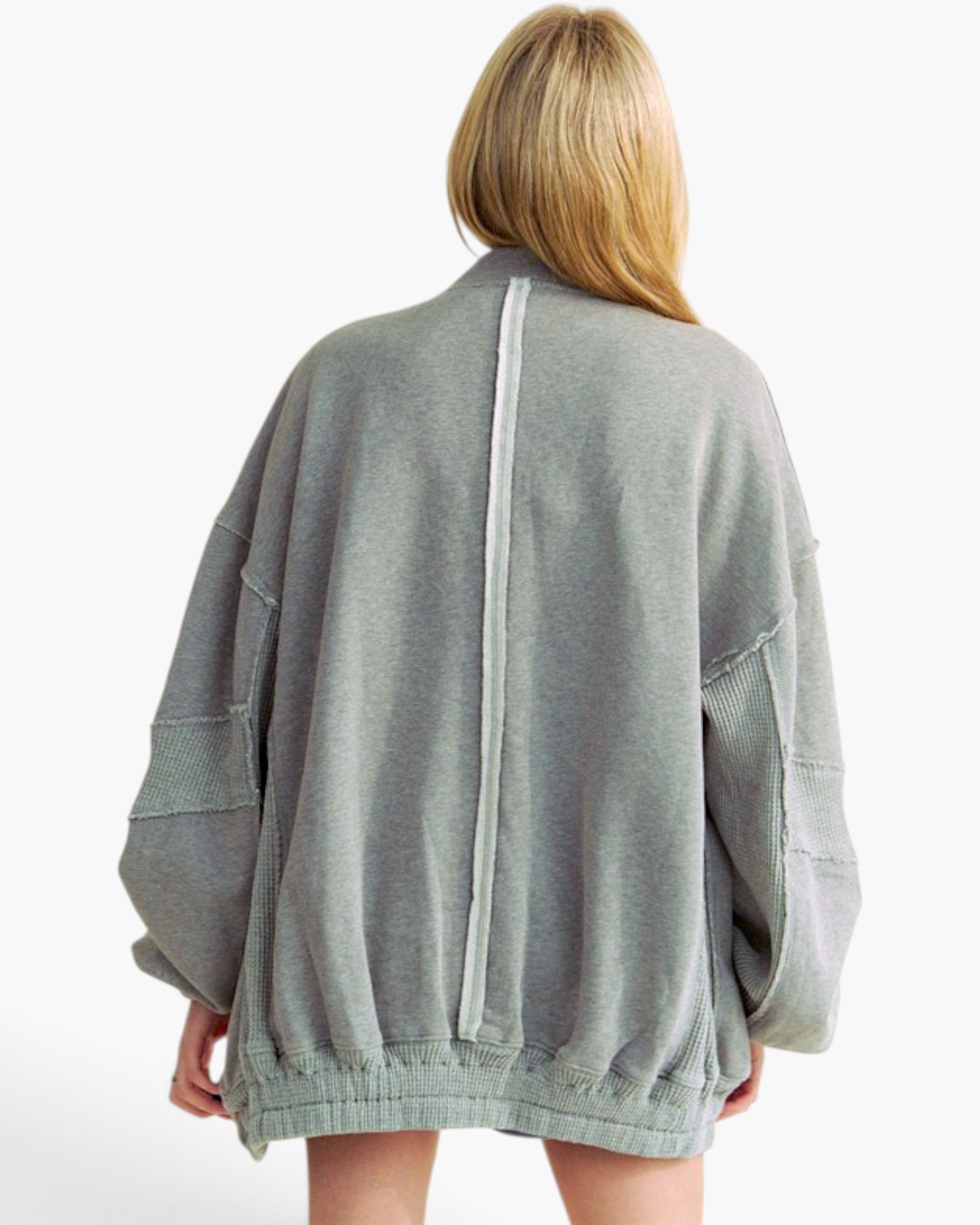 A woman viewed from behind wearing an oversized light gray jacket with a central vertical seam and patch pockets, against a plain white background.