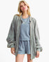 A woman modeling a light sage green corduroy zip-up jacket over a dusty blue polka-dot lounge set, photographed against a clean white background.