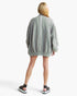 A woman shown from the back wearing an oversized light gray knit sweater with a prominent white vertical stripe down the center back, set against a plain light gray studio background.