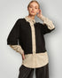 Woman wearing a black and beige outfit with a plain background