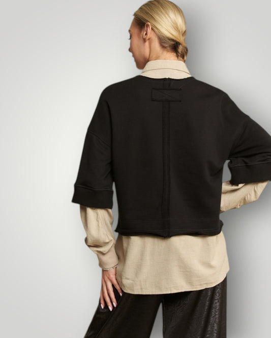 Person wearing a black jacket over a beige shirt with a plain background