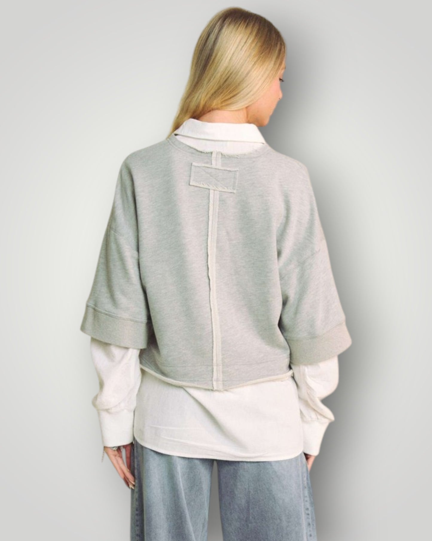 Person wearing a light gray jacket over a white shirt with a plain background