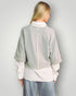 Person wearing a light gray jacket over a white shirt with a plain background