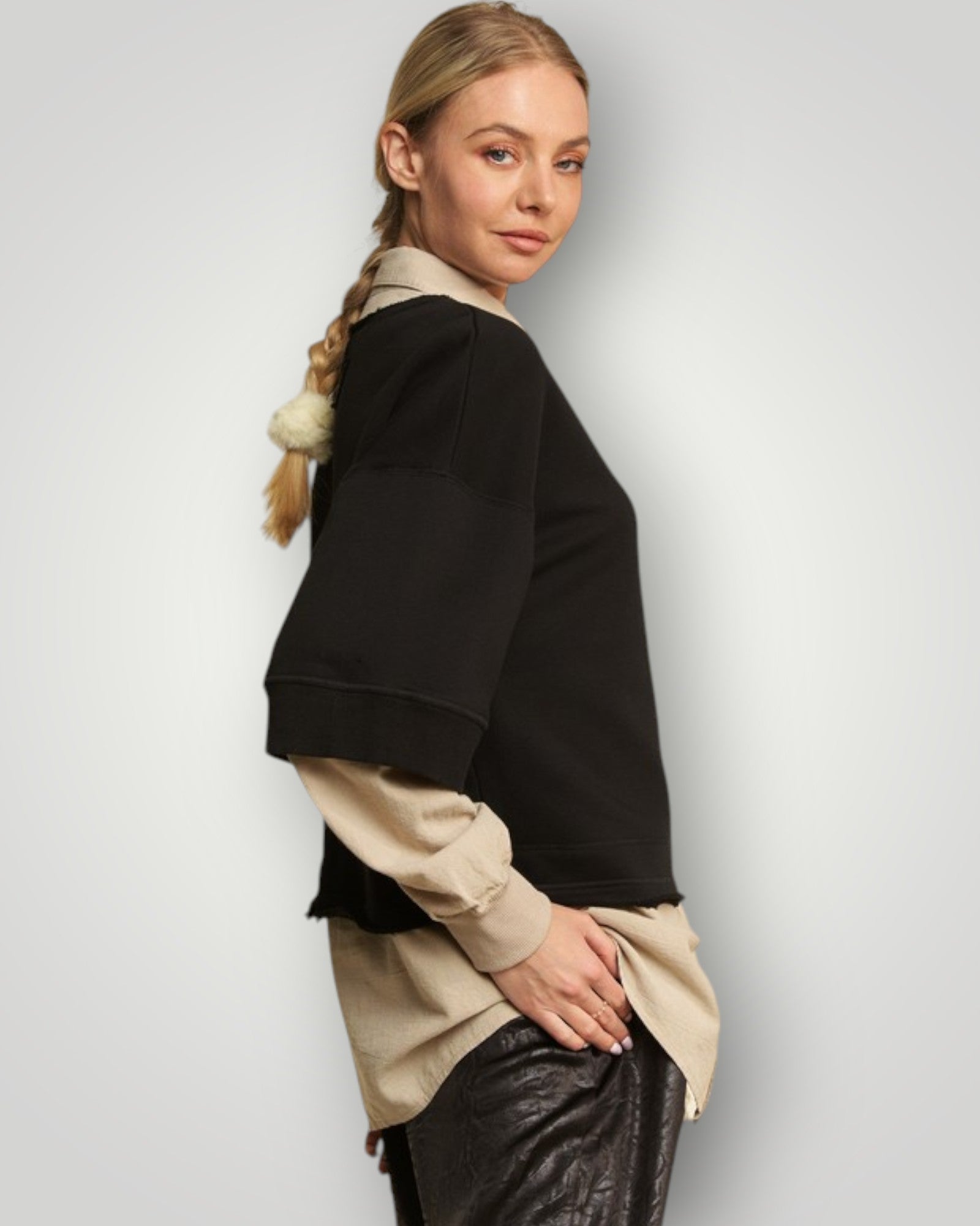 Woman wearing a black and beige outfit with leather pants on a light gray background