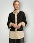 Woman wearing a black and beige two-tone shirt against a plain background