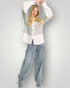 Woman wearing a layered outfit with a white shirt, green cardigan, and blue jeans on a plain background