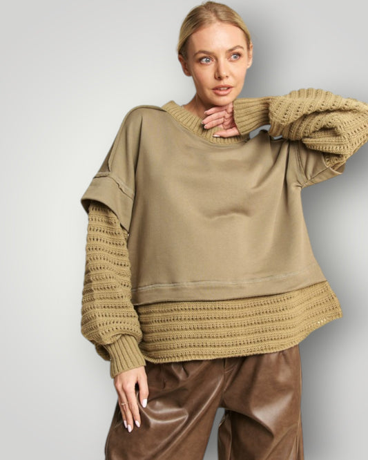 Woman wearing a beige sweater with textured sleeves against a light gray background