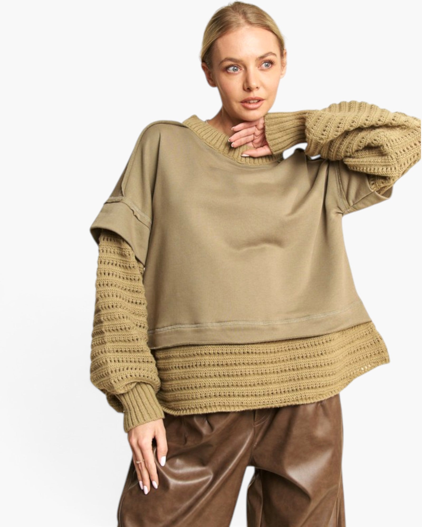 A woman modeling a loose-fit knit sweater with a solid taupe-brown body and ribbed knit sleeves and hem, paired with brown faux-leather pants against a plain white background.