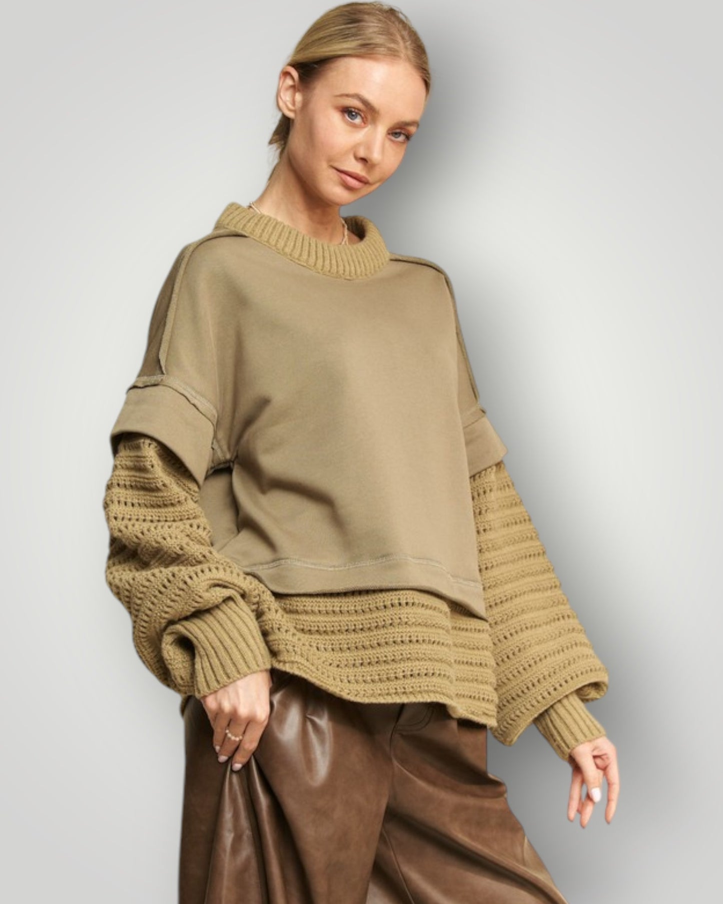 Woman wearing a beige sweater with textured sleeves against a plain background