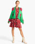 A model wearing a festive holiday-themed outfit featuring a bright green knit cardigan with red floral appliques, a red and pink floral mini dress, and cream lace-up ankle boots, set against a plain white studio background.