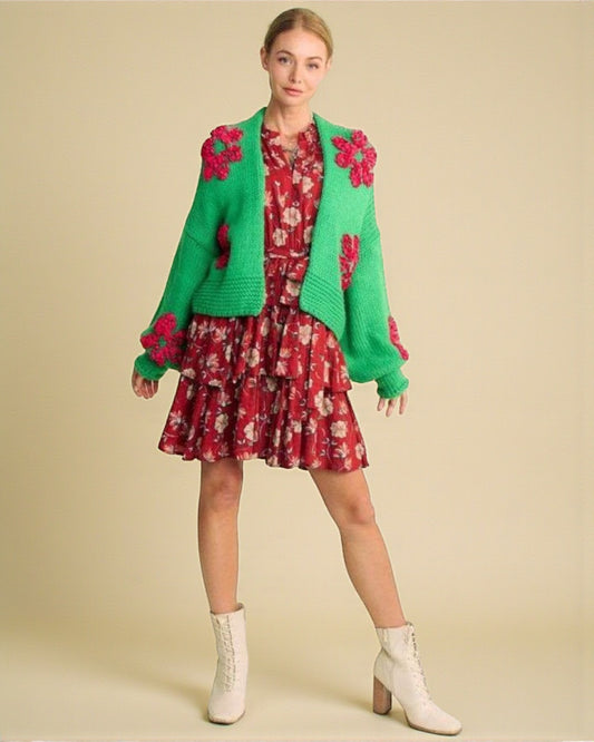 Woman wearing a green cardigan with floral patterns over a red floral dress on a beige background