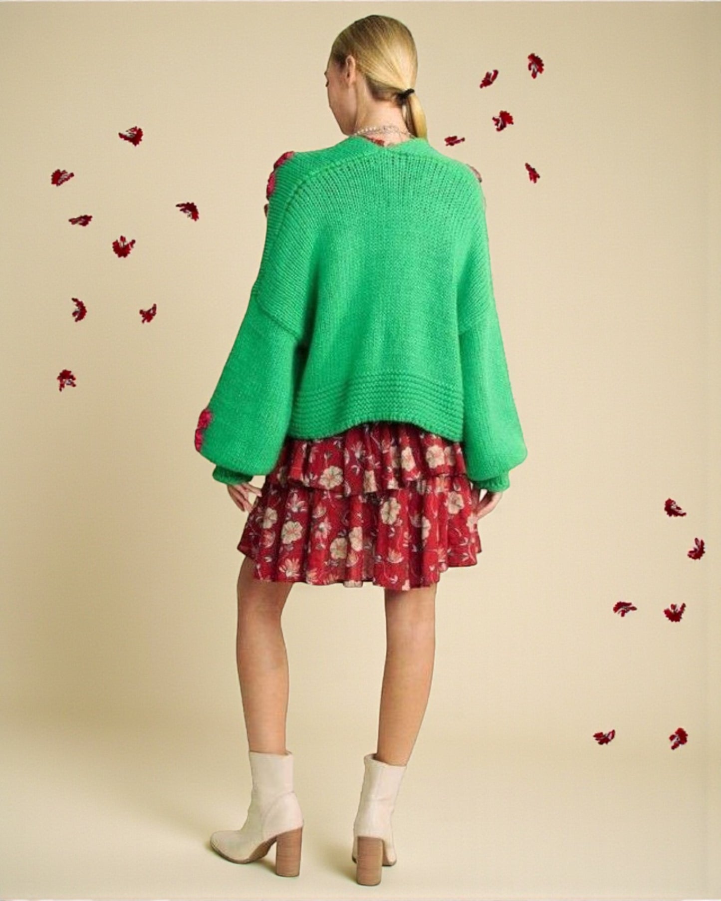 Woman wearing a green cardigan over a red floral dress on a beige background with red flower petals.