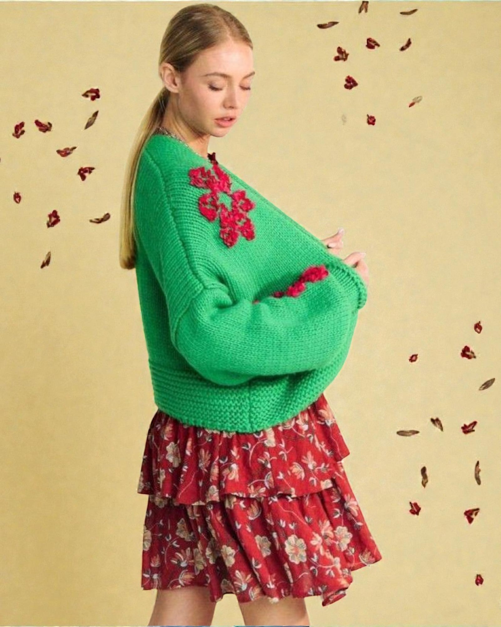 Woman wearing a green sweater with floral patterns and a red floral skirt on a beige background.