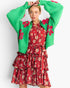 A woman modeling a bright green knit cardigan with pink floral embroidery over a red tiered floral dress, posed against a light gray studio background.