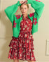 Woman wearing a green cardigan with floral patterns and a red floral dress against a beige wall.
