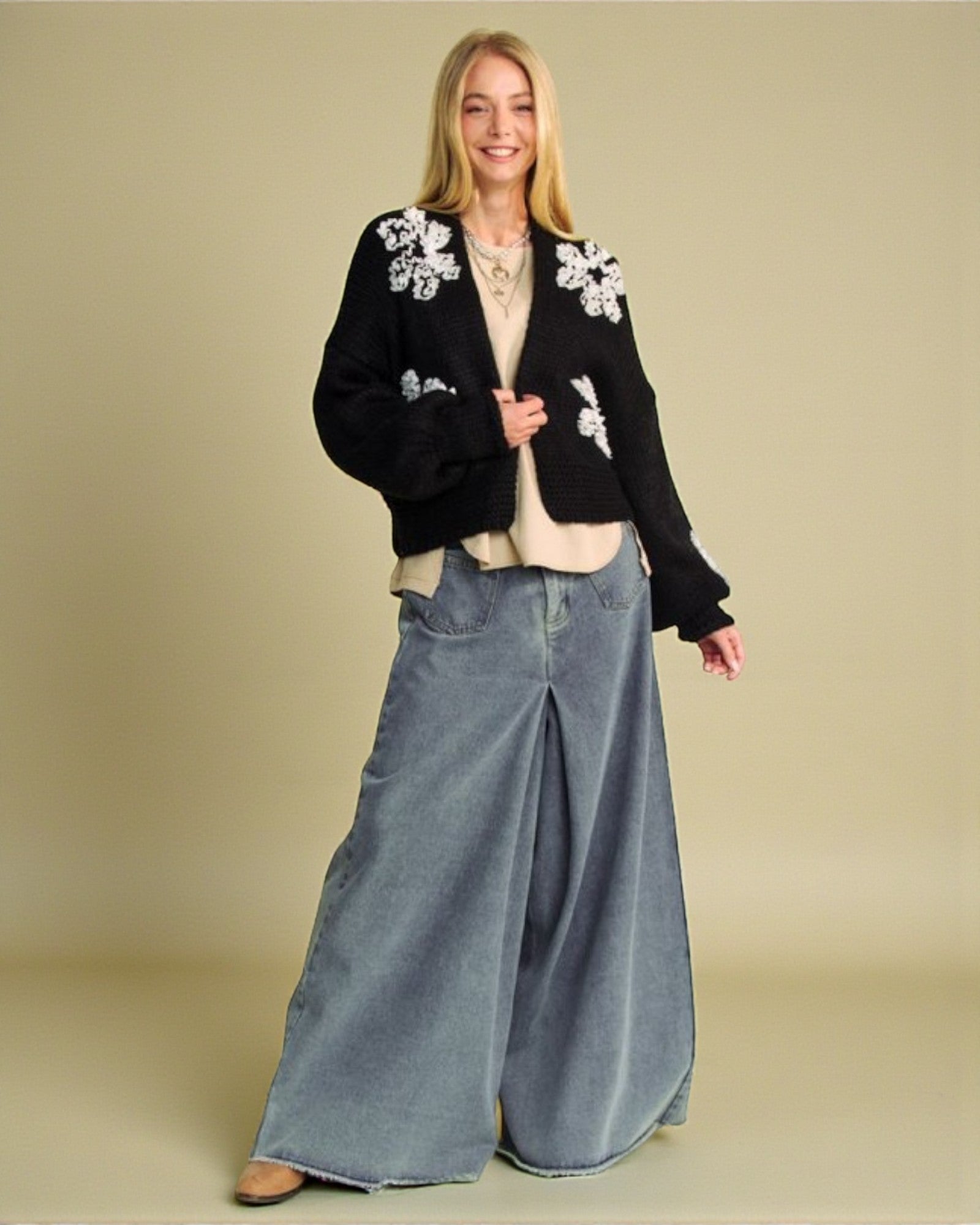 Woman wearing a black floral cardigan and blue jeans on a beige background