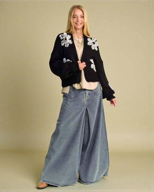 Woman wearing a black floral cardigan and blue jeans on a beige background