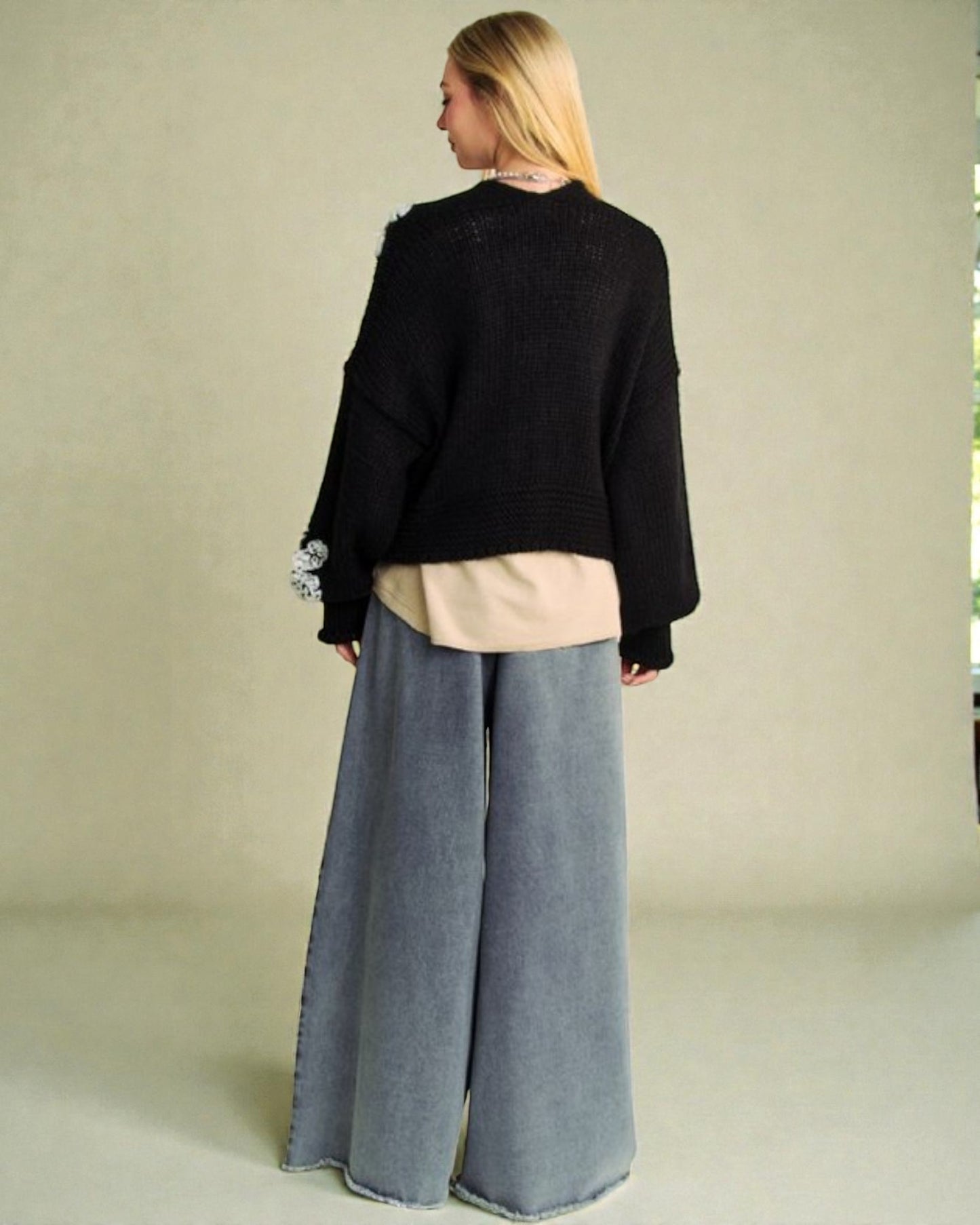 Person wearing a black sweater and gray wide-leg pants against a neutral background